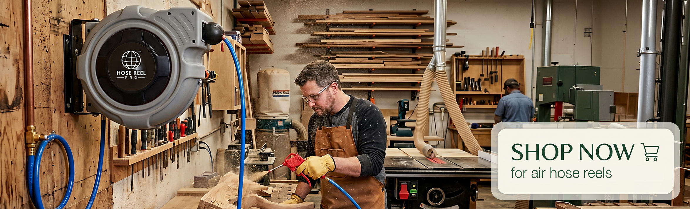 Woodworker in apron sands a piece of wood in a busy shop, with tools on the wall and a large hose reel visible to the left.
